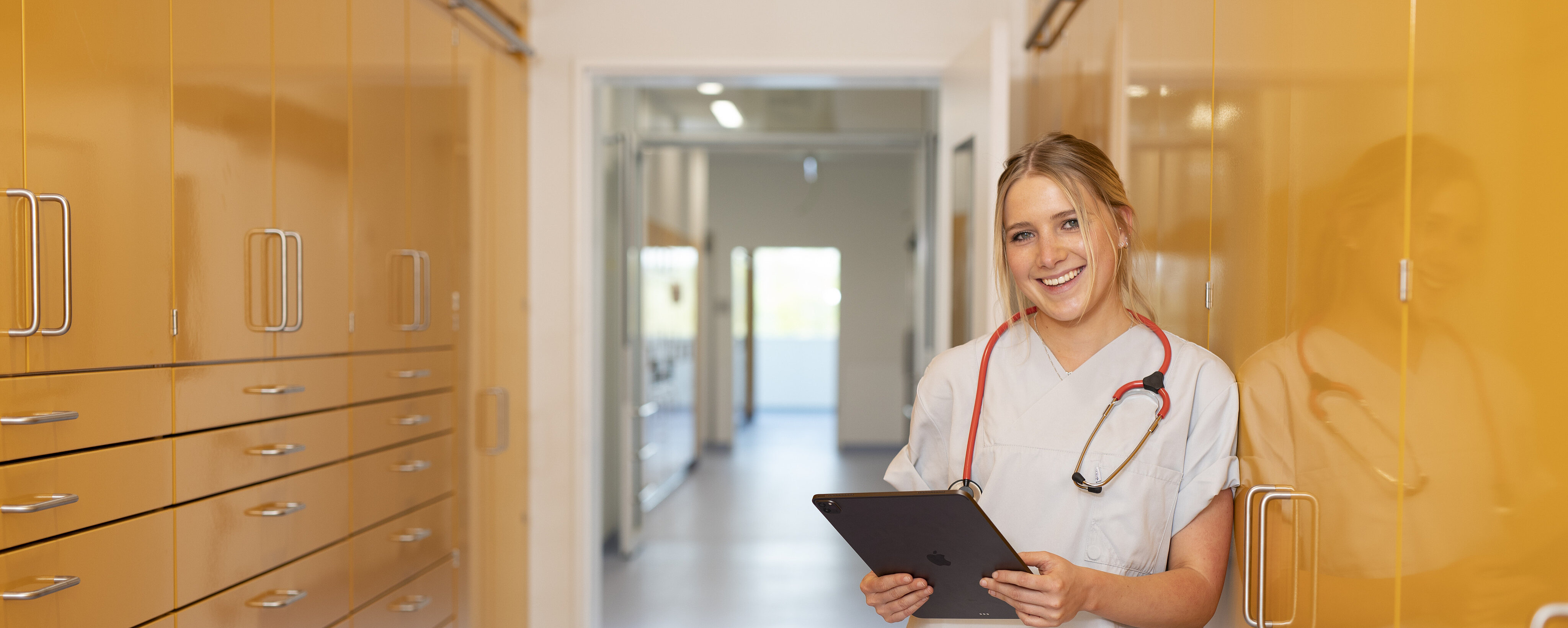 lächelnde Krankenschwester mit Stethoskop um den Hals lehnt sich an einen Schrank