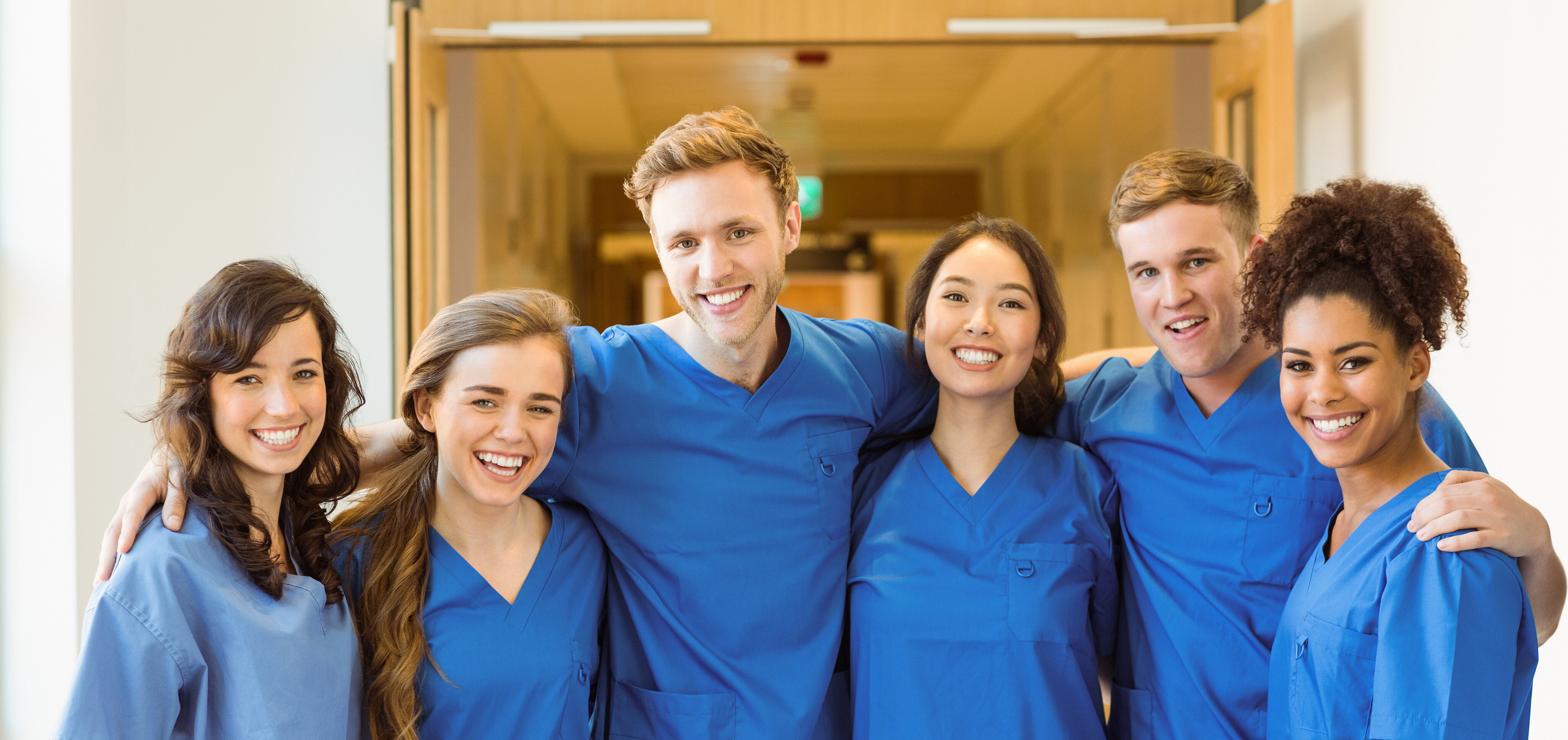 Sechs Klinikmitarbeiter mit blauen Kasaks stehen nebeneinander und umarmen sich