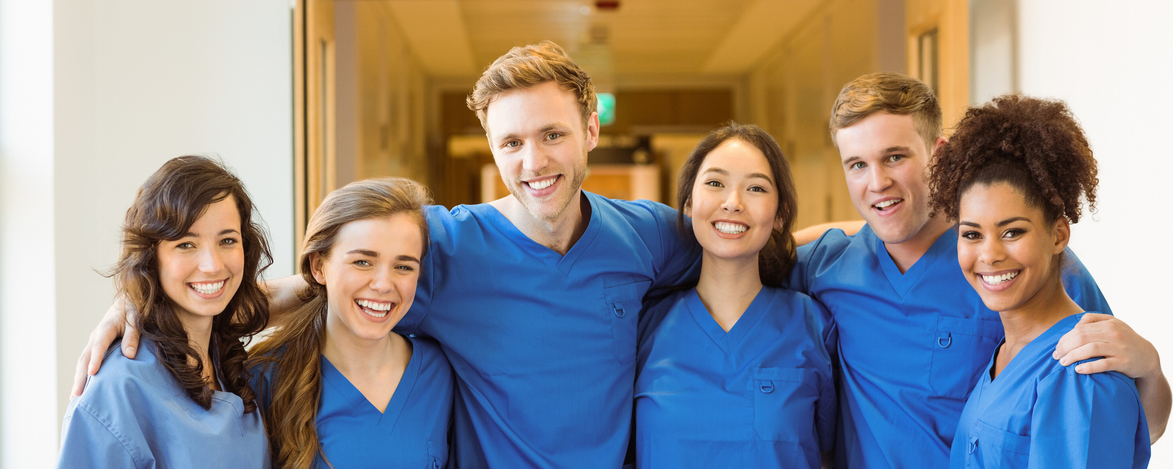 Sechs Klinikmitarbeiter mit blauen Kasaks stehen nebeneinander und umarmen sich