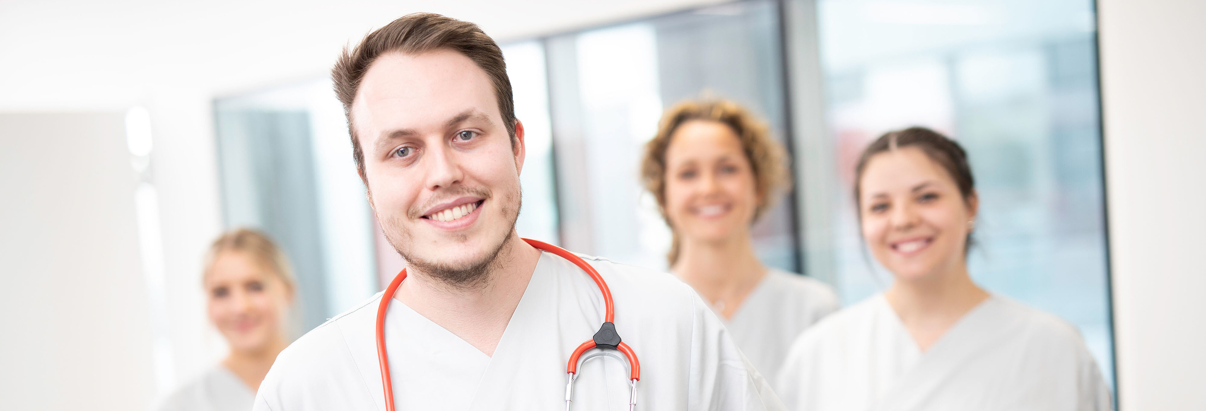 Ein Pfleger mit Stethoskop im Vordergrund, im Hintergrund 3 Schwestern