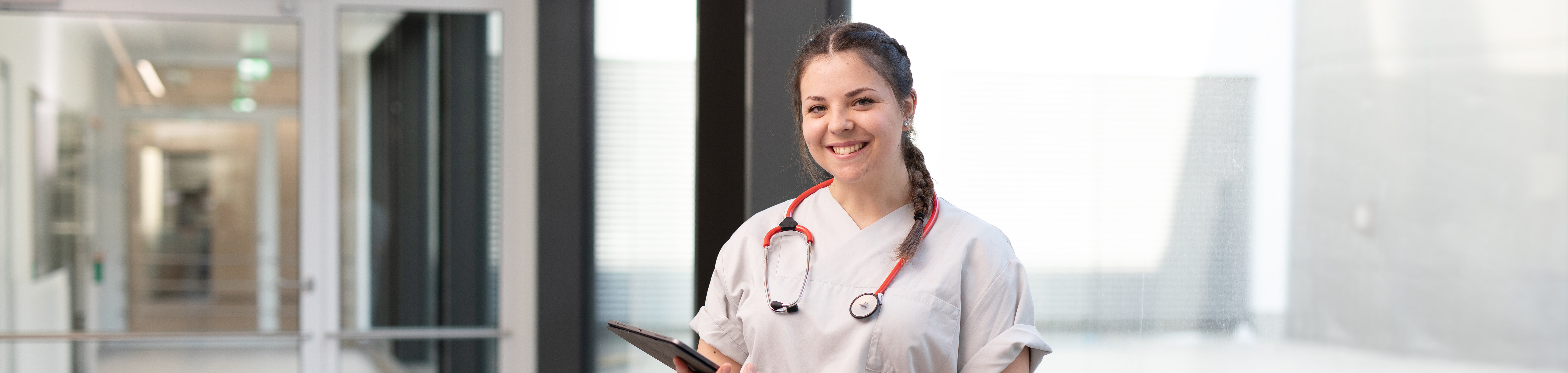lächelnde Krankenschwester mit Stethoskop steht im Gang