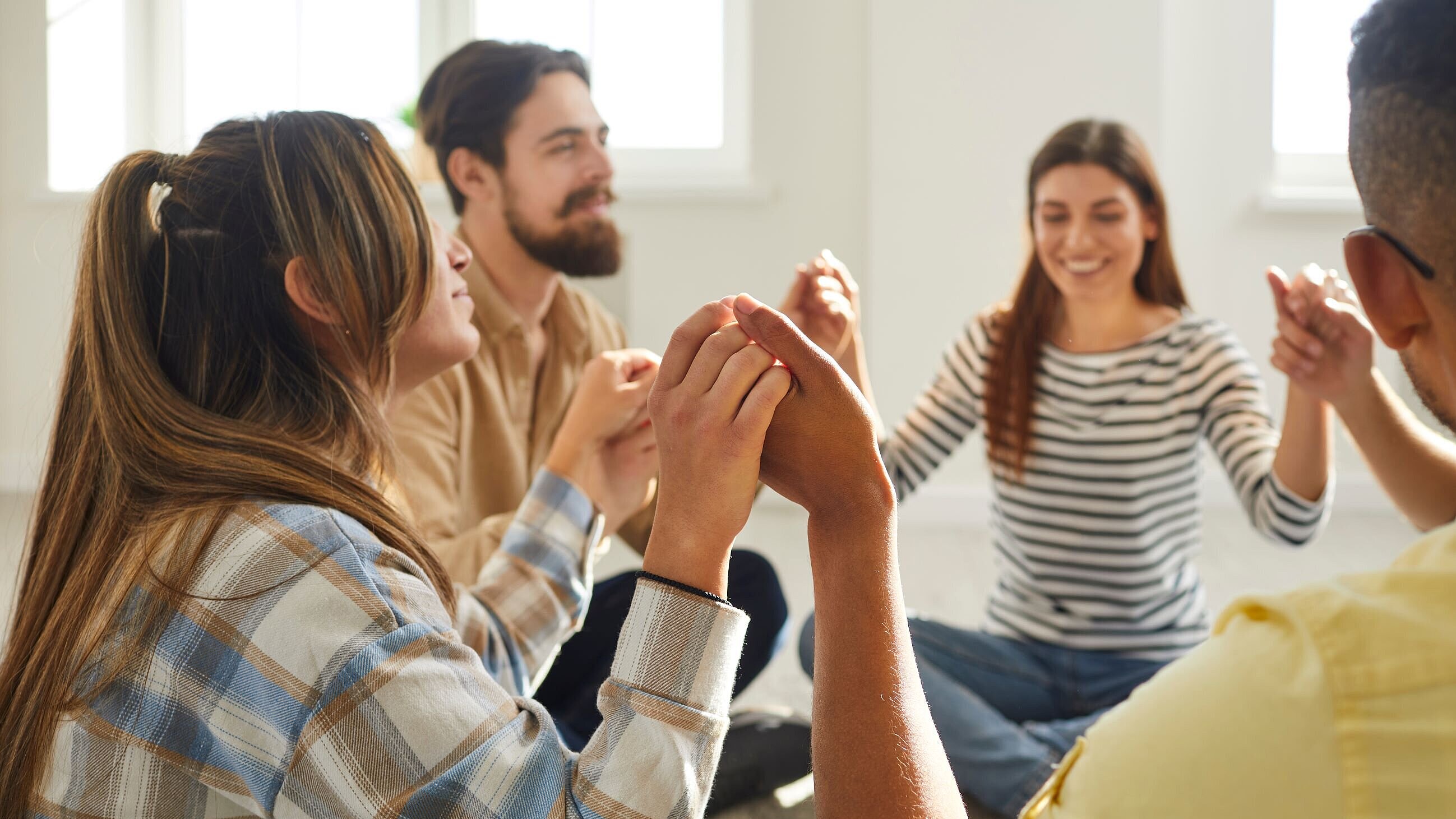 jungen Menschen im Sitzkreis geben sich die Hand