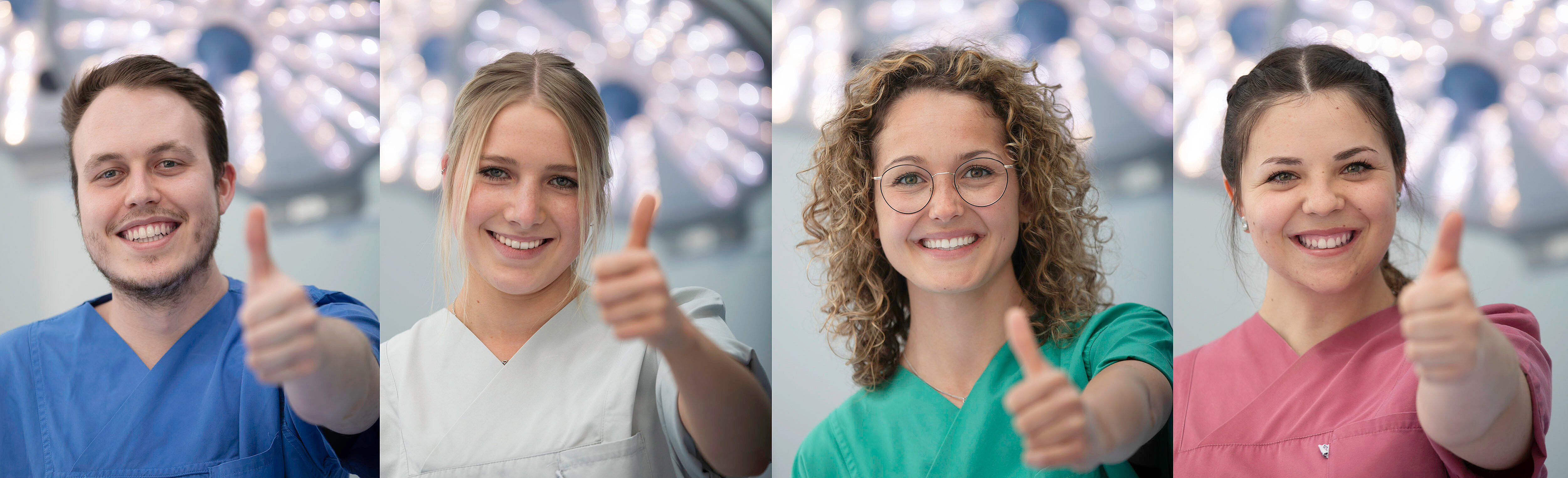 vier Auszubildende in verschiedenfarbiger Dienstkleidung lachen und halten den Daumen nach oben.