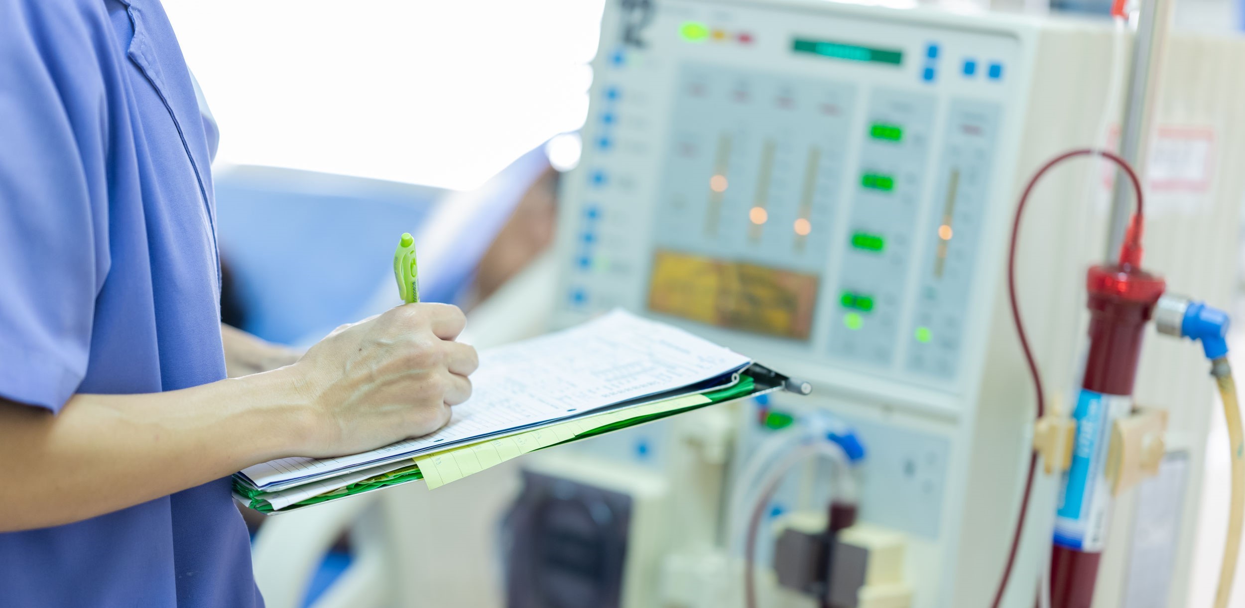 Pflegekraft steht vor Dialysegerät und dokumentiert die Werte