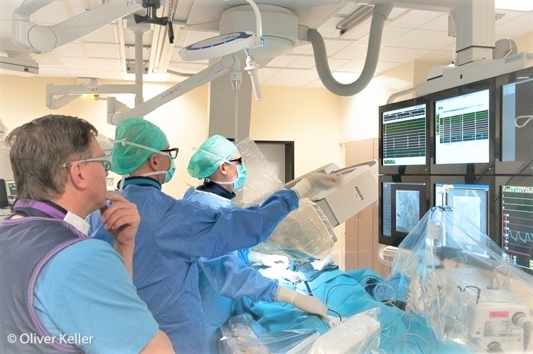 Szene aus dem Herzkatheter: Drei Ärzte stehen vor den Röntgenbildschirmen