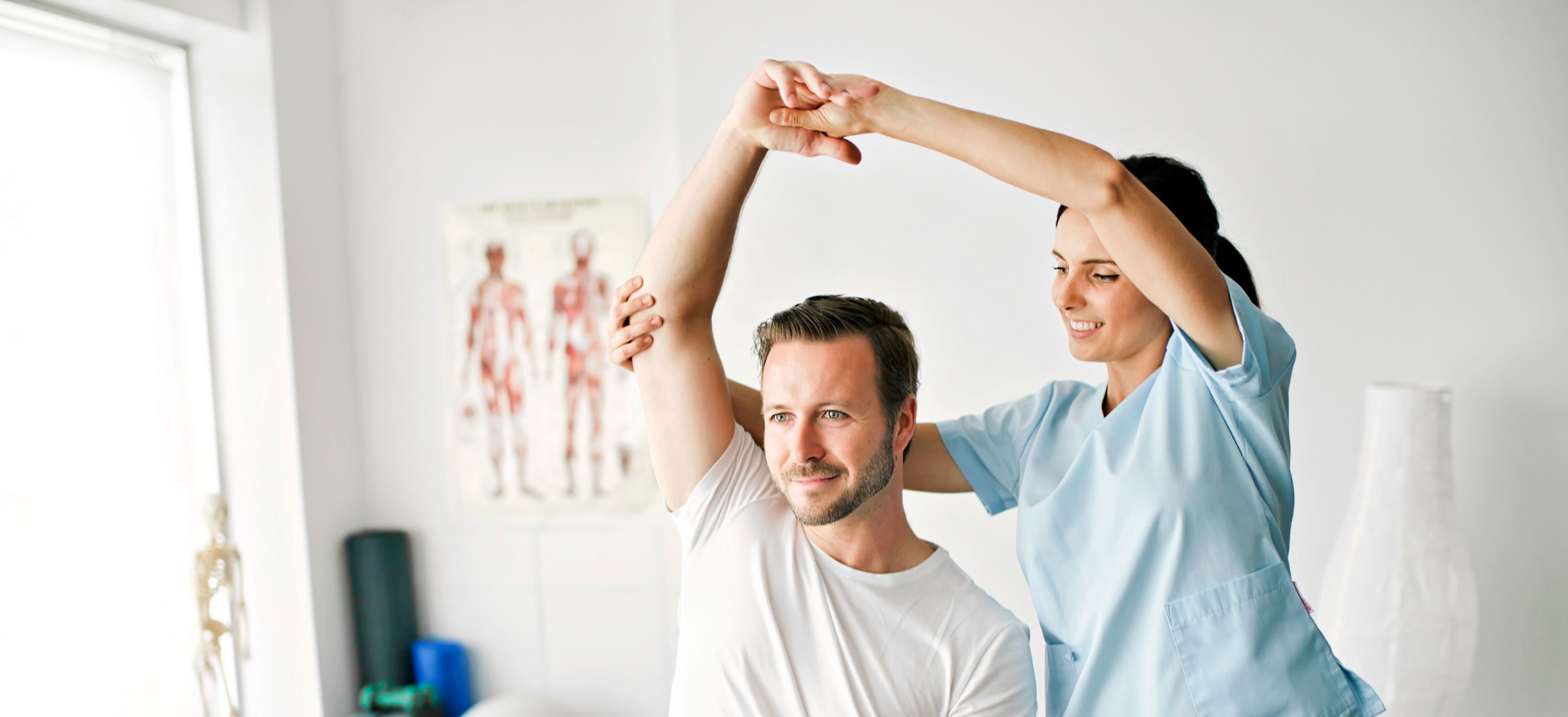 Patient sitzt, Physiotherapeutin steht hinter Patienten und streckt den rechten Arm des Patienten nach oben